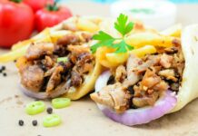 Traditiona Greek pita gyros with meat, fried potatoes, tomato, onion and drink on brown Paper, Placed on blue Wooden Table